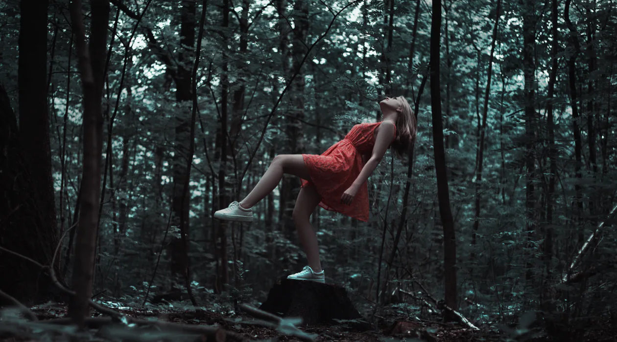 A woman in the woods jumping off of a platform.