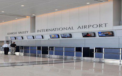 A large airport terminal with many monitors on the wall.