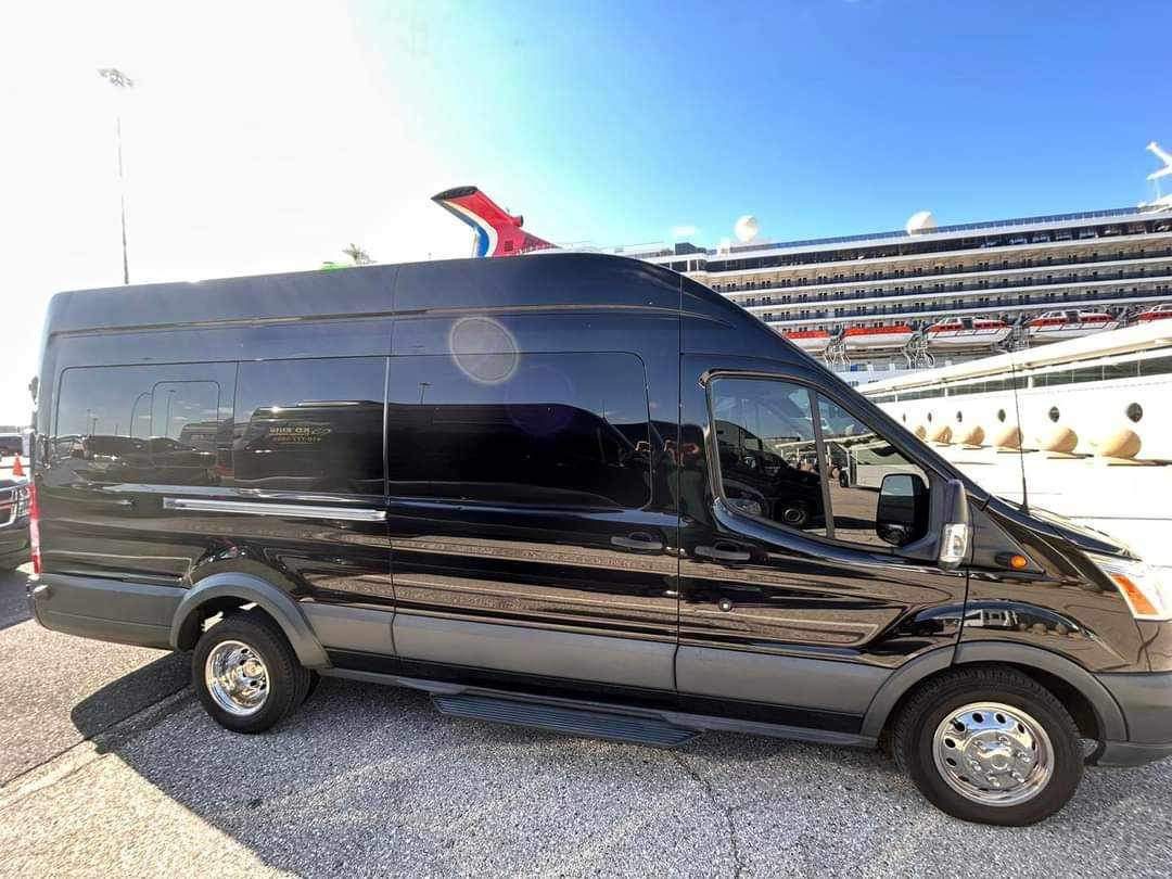 A black van parked in front of a cruise ship.