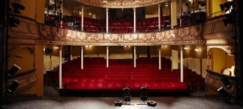 A theater with red seats and two black chairs.